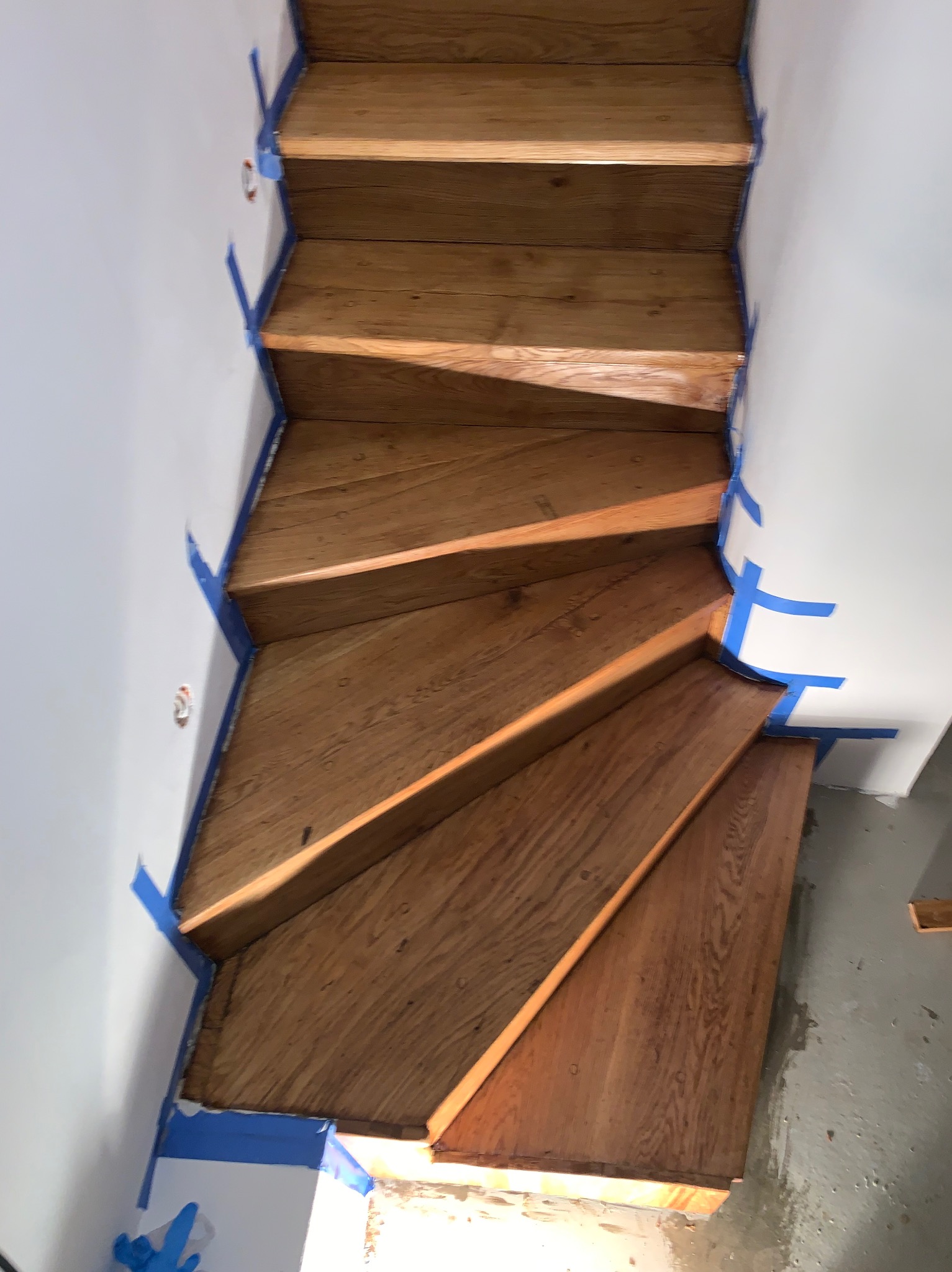 Drewniane schody zabezpieczone taśmą malarską przed malowaniem ścian. Widoczne detale usłojenia drewna i precyzyjne oklejenie krawędzi. Ujęcie z góry.