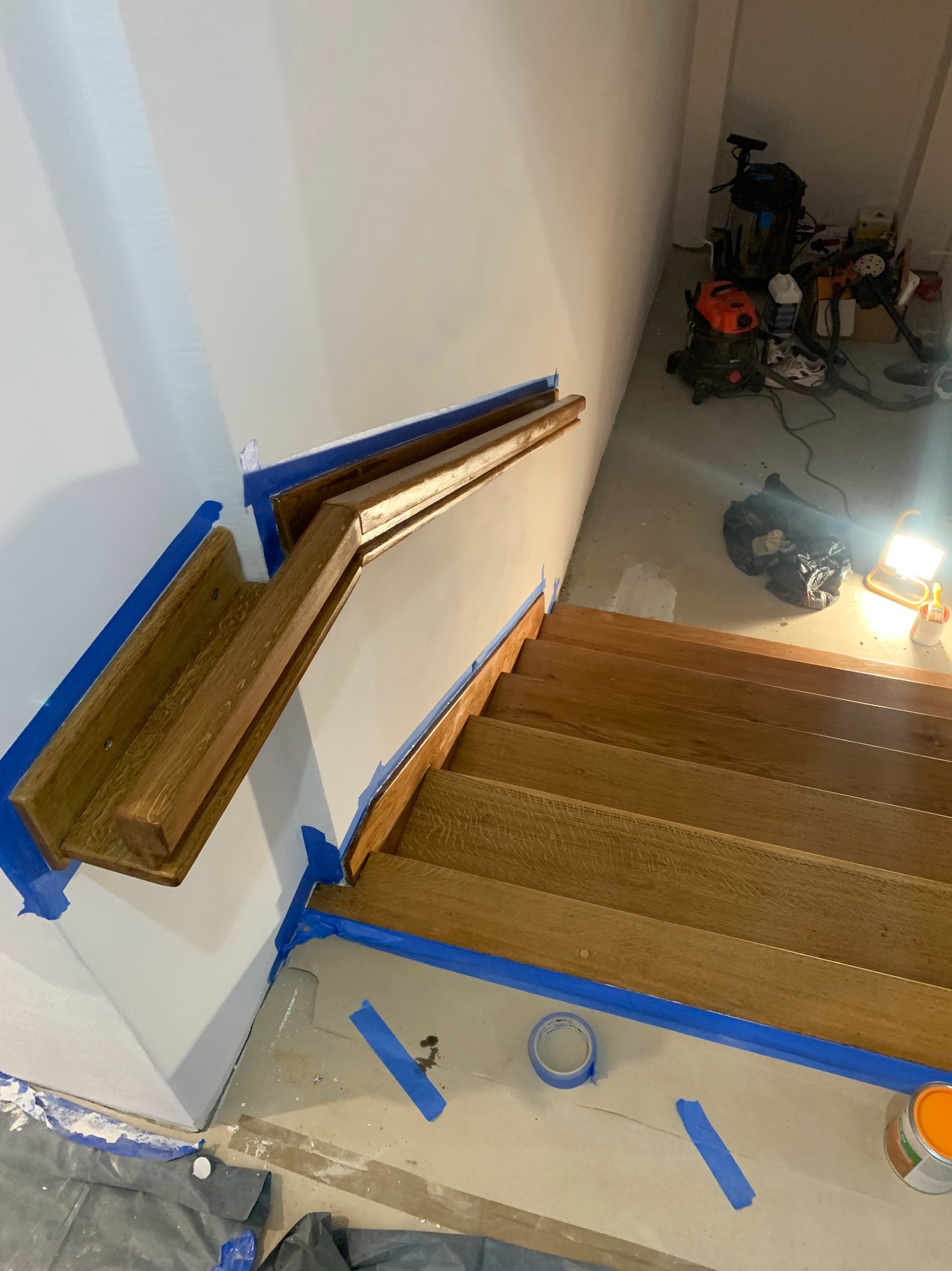 Drewniane schody z zabezpieczeniem taśmą malarską, świeżo pomalowane ściany, widoczne narzędzia i akcesoria malarskie. Ujęcie z góry, podkreślające detale wykończenia.