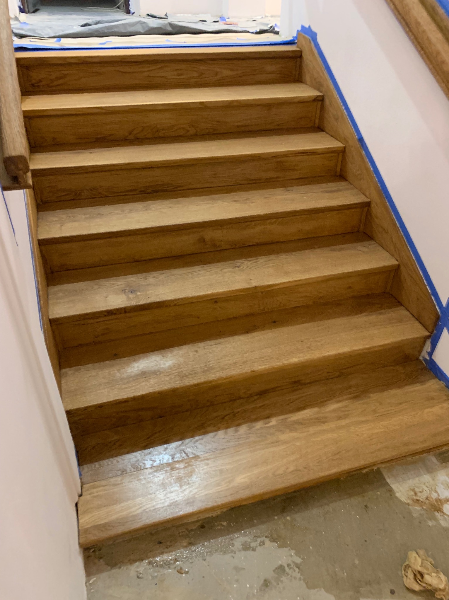 Odnowione drewniane schody z zabezpieczonymi taśmą malarską ścianami. Widoczne ślady prac wykończeniowych na podłodze.