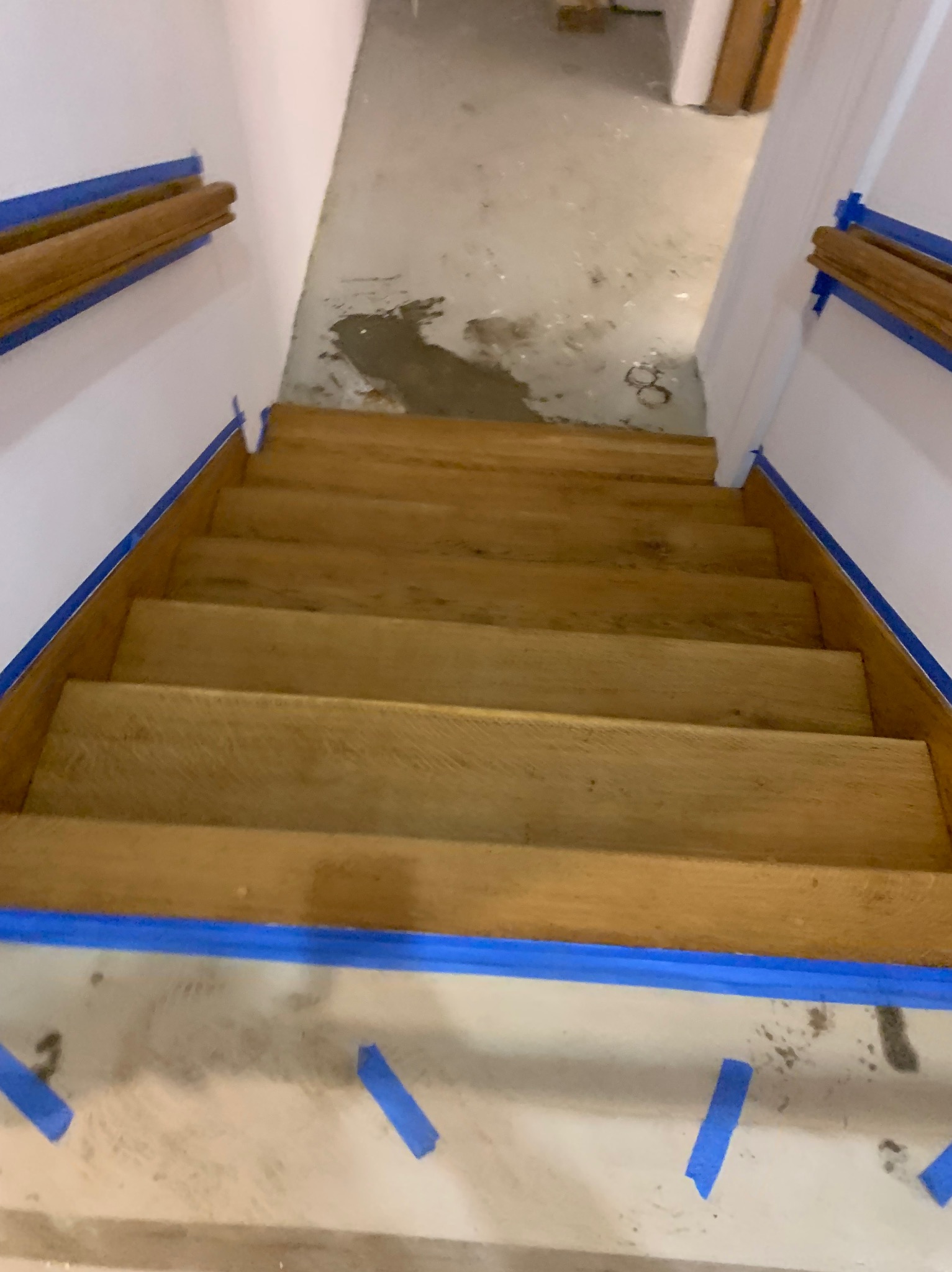 Drewniane schody po renowacji, zabezpieczone taśmą malarską, widok z góry. Usługa wykonana w Warszawie. Jasne drewno, białe ściany.