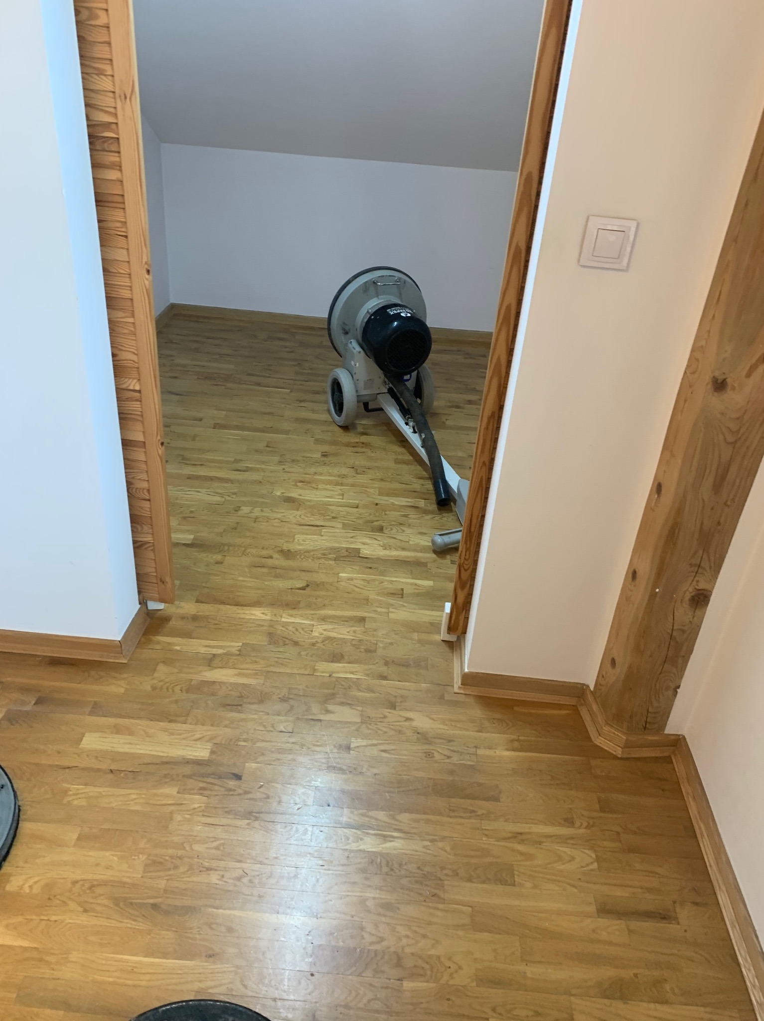 Cyklinowanie parkietu w trakcie realizacji: maszyna do cyklinowania na drewnianej podłodze, widoczne detale wykończenia ścian i listew przypodłogowych.