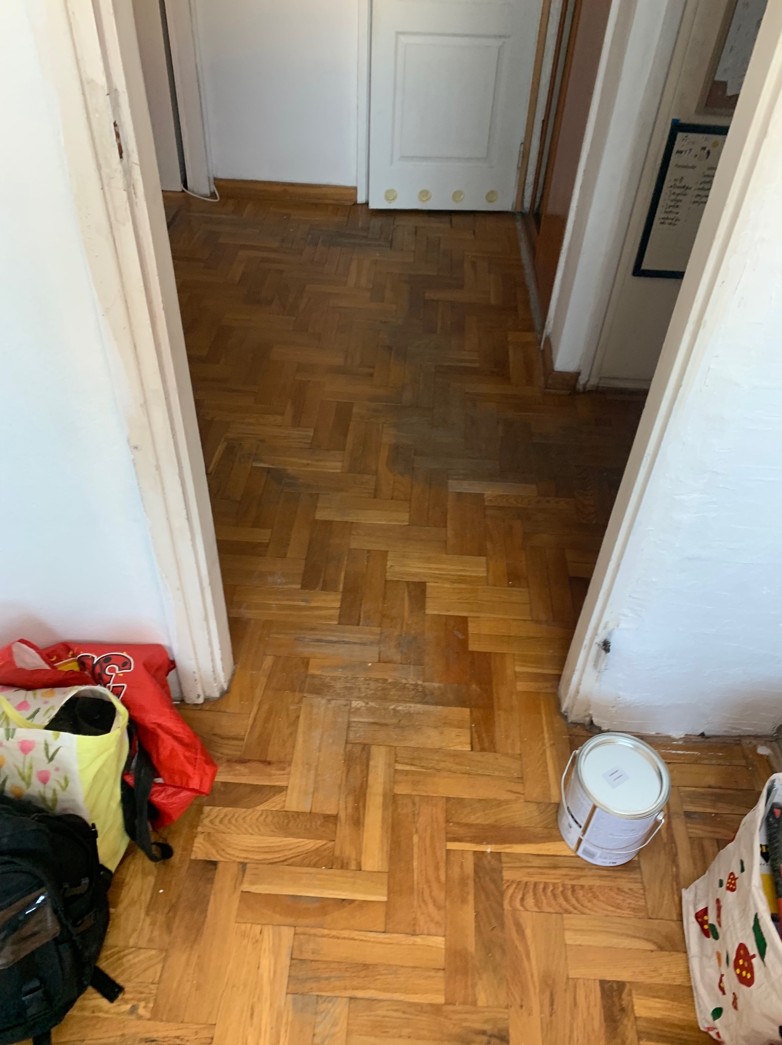 Parkiet ułożony w jodełkę, częściowo wycyklinowany, z widocznymi śladami użytkowania i puszką farby w rogu. Widok z góry na fragment podłogi w trakcie renowacji.