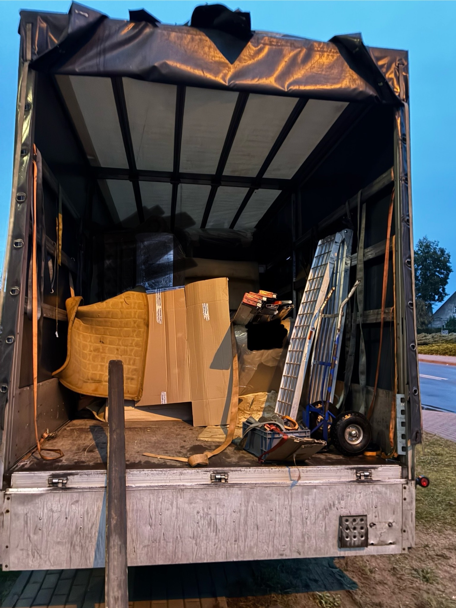 Wnętrze skrzyni ładunkowej samochodu dostawczego wypełnionej kartonami, dywanem i drabiną, przygotowanego do transportu podczas opróżniania mieszkania.