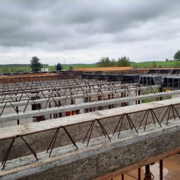 HOVERLA LTD - Zbrojenie stropu w trakcie budowy domu, widoczne szalunki i stalowe pręty, w tle zielony krajobraz pod pochmurnym niebem.