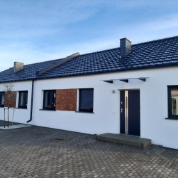 HOVERLA LTD - Szeregowy budynek mieszkalny z białymi ścianami, ciemną dachówką i stolarką okienną, wykończony elementami drewnianymi i z kostki brukowej na podjeździe.