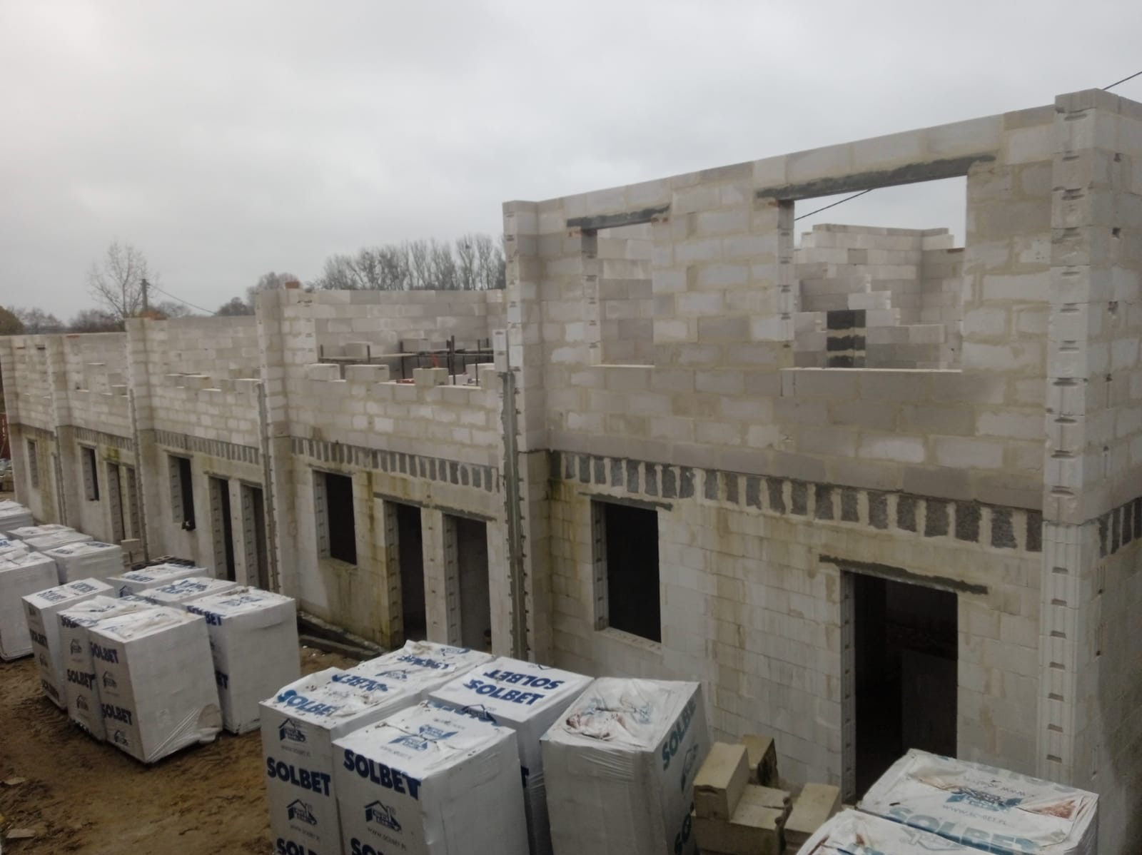 Wznoszone ściany szeregówki z betonu komórkowego, widoczne pakiety bloczków Solbet na placu budowy, otwory okienne i drzwiowe w trakcie murowania.