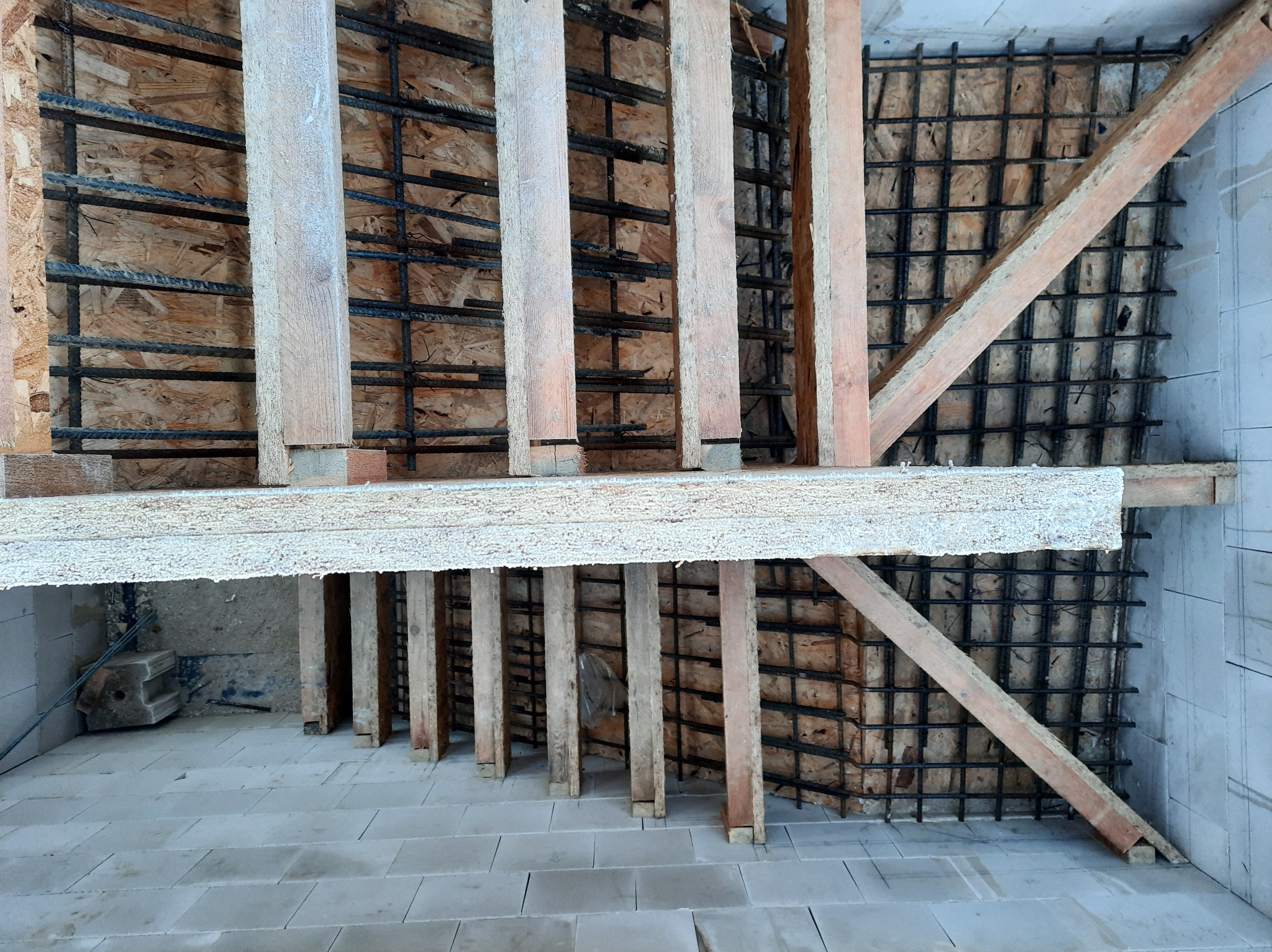 Szczegół konstrukcji szalunku fundamentu z drewnianymi stemplami i siatką zbrojeniową na płycie OSB, widok z dołu.