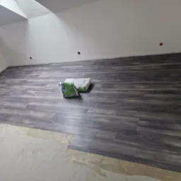 Układanie paneli podłogowych w poddaszu, widoczne worki z klejem i fragment ściany w stanie surowym.