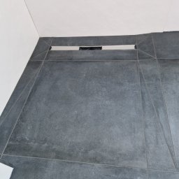 Majer-bau - Szare płytki podłogowe w łazience z odpływem liniowym przy ścianie, widok z góry.