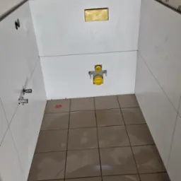 Białe płytki ścienne i brązowe płytki podłogowe w trakcie układania, widoczne elementy instalacji sanitarnej i poziomica.