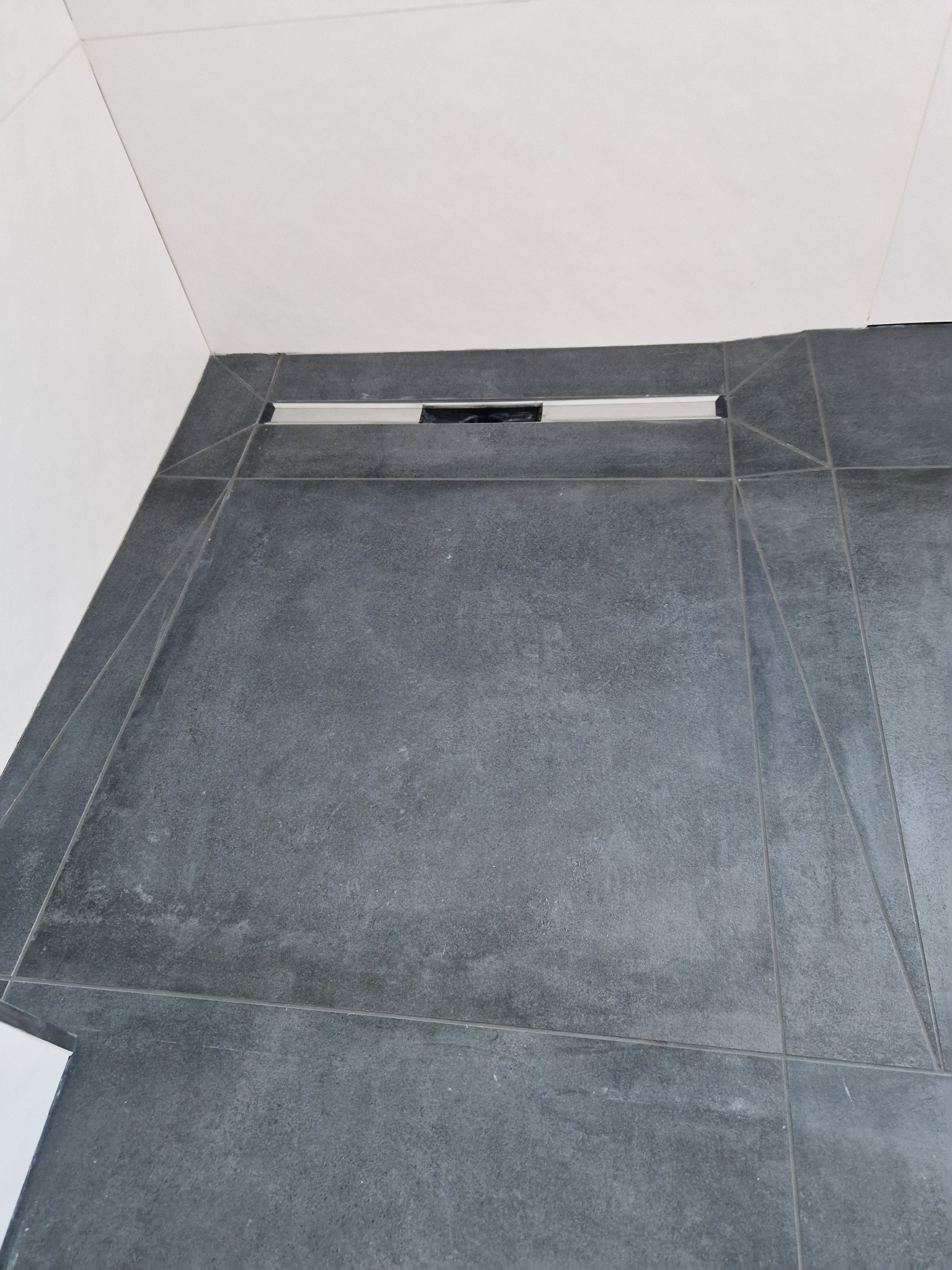 Szare płytki podłogowe w łazience z odpływem liniowym przy ścianie, widok z góry.