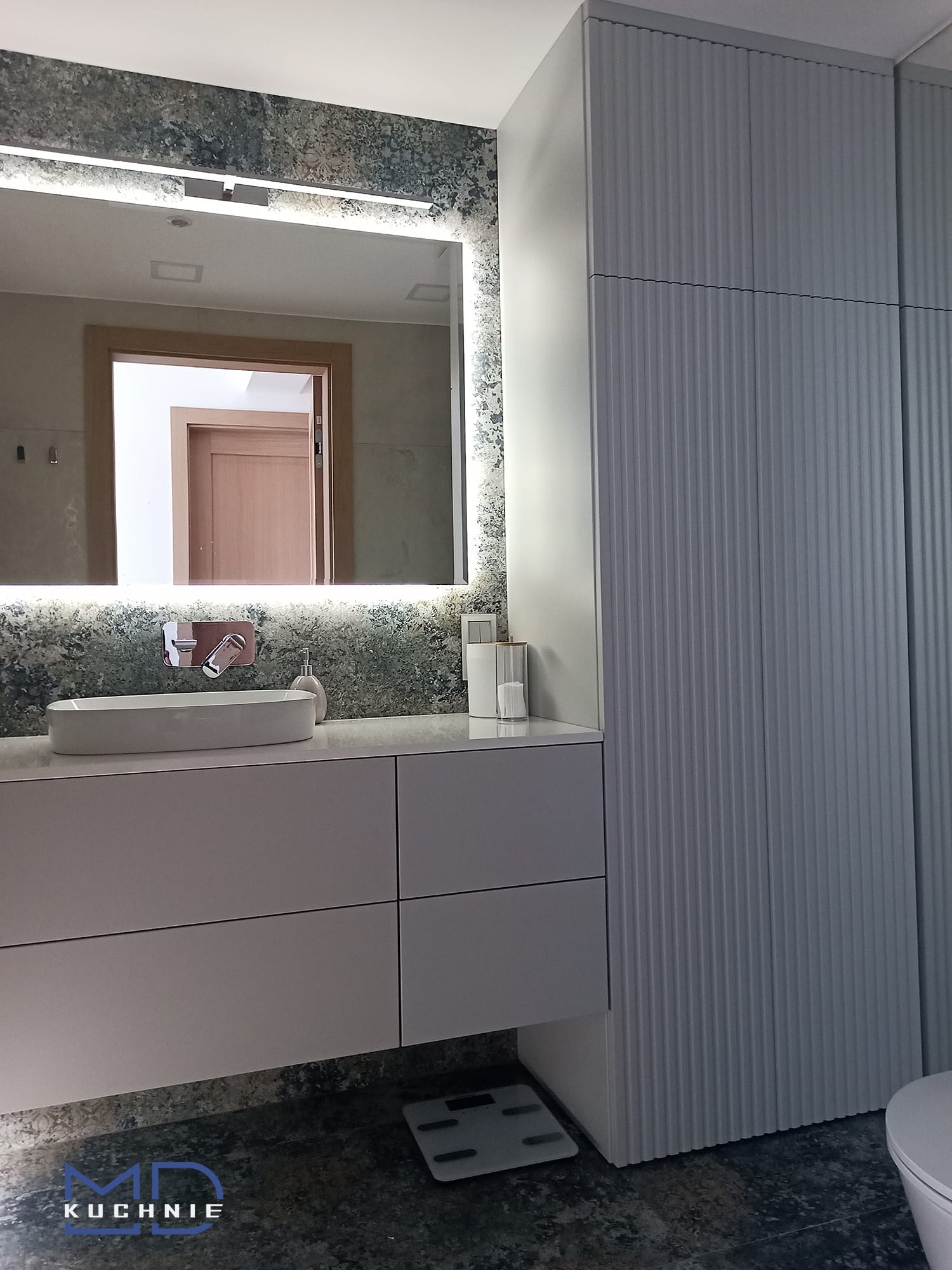 Nowoczesna łazienka w Kaniowie z umywalką nablatową, podświetlanym lustrem i szafką z frezowanymi frontami, uzupełniona o wagę łazienkową.