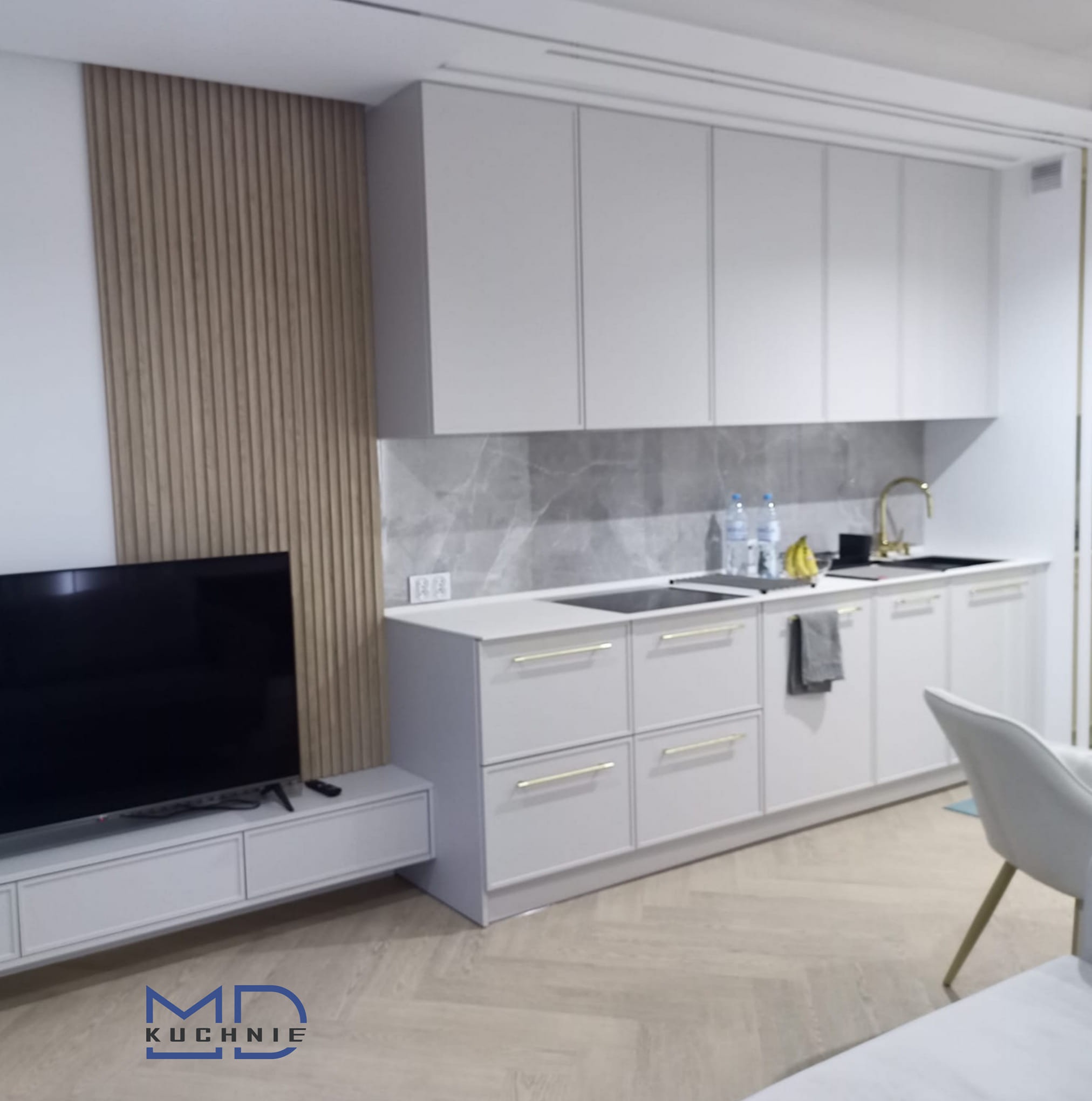 Nowoczesna, minimalistyczna kuchnia w odcieniach szarości z drewnianą ścianką działową, złotymi akcentami i podłogą w jodełkę.