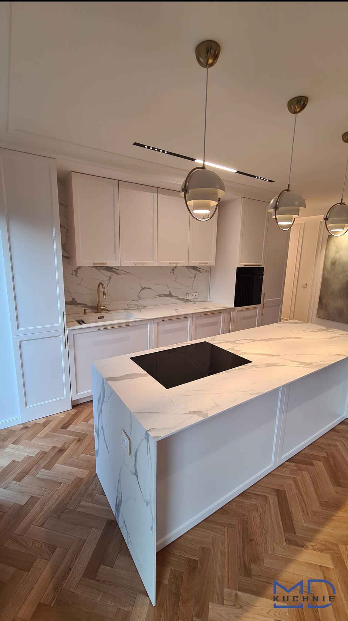 Elegancka, jasna kuchnia z wyspą i marmurowym blatem, złota armatura, parkiet w jodełkę, oświetlenie punktowe