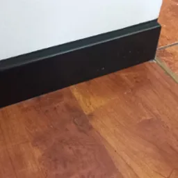 Połączenie podłóg: panele imitujące drewno i terakota oddzielone złotą listwą, czarna listwa przypodłogowa przy białej ścianie.