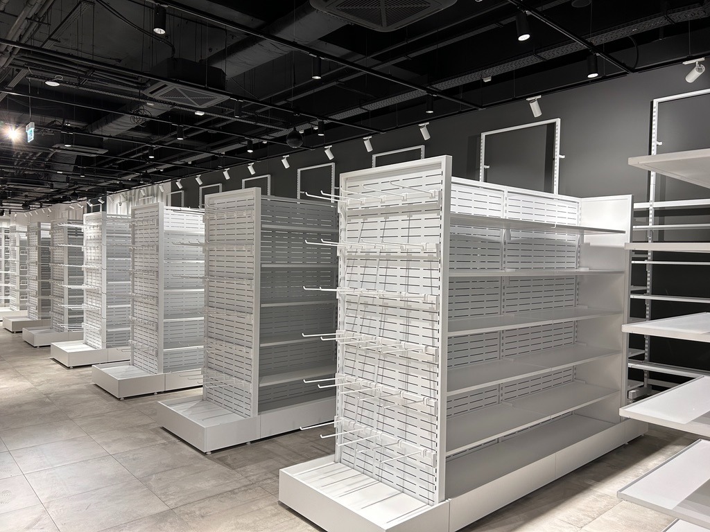 Wnętrze sklepu SINSAY w centrum handlowym Sofia Ring Mall, Bułgaria, prezentujące rząd białych, metalowych regałów z otworami i haczykami, ustawionych na szarej podłodze z płytek, z czarnym sufitem...