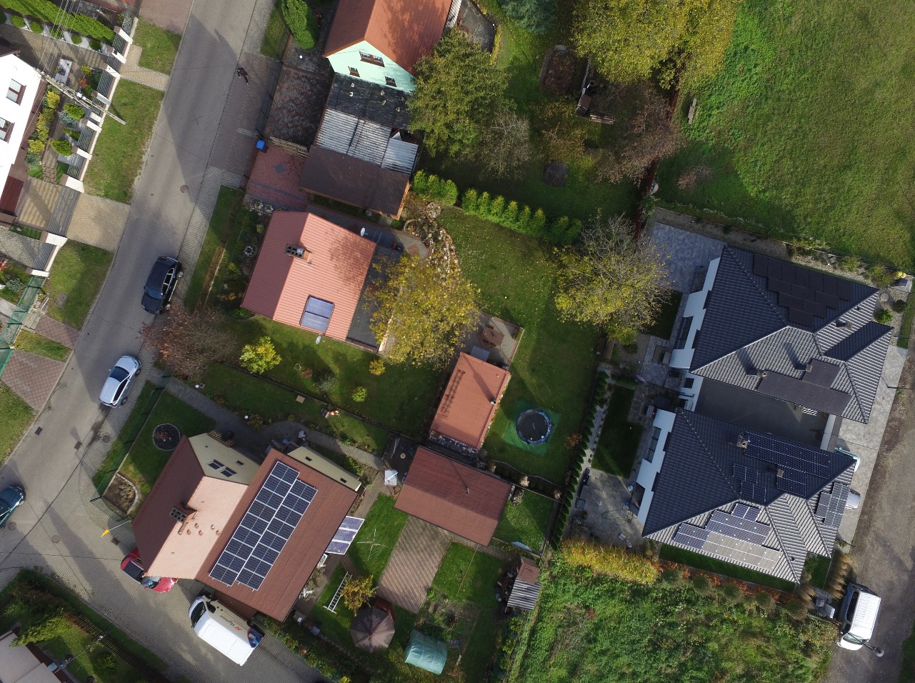 Widok z lotu ptaka na osiedle domów jednorodzinnych z panelami słonecznymi na dachach, otoczone zielenią i drogami.