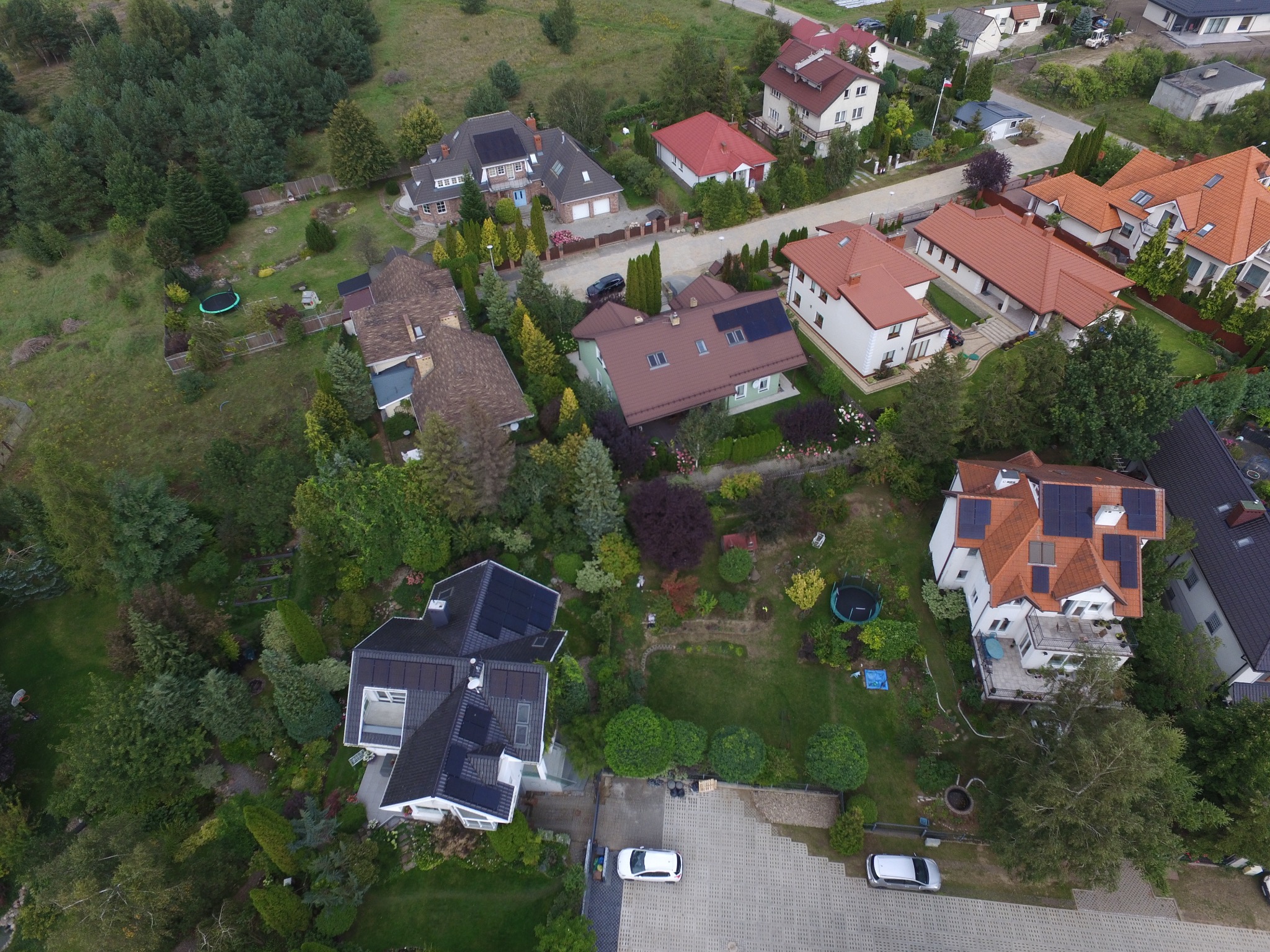 Widok z lotu ptaka na osiedle domów jednorodzinnych z panelami słonecznymi na dachach, otoczonych zielenią i ogrodami.
