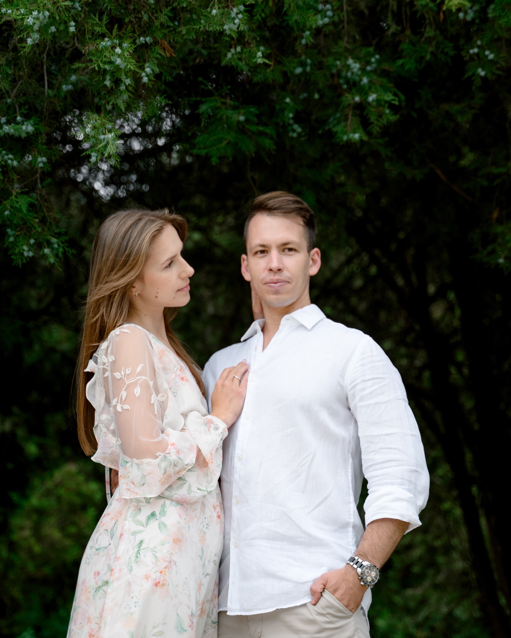 Para zakochanych: kobieta w kwiecistej sukience opiera dłoń na ramieniu mężczyzny w białej koszuli, oboje stoją na tle zieleni