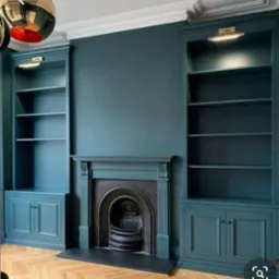 Elegancki salon z zabudowanymi regałami i kominkiem w odcieniach morskiej zieleni, parkiet w jodełkę, oświetlenie punktowe nad półkami, minimalistyczny design.