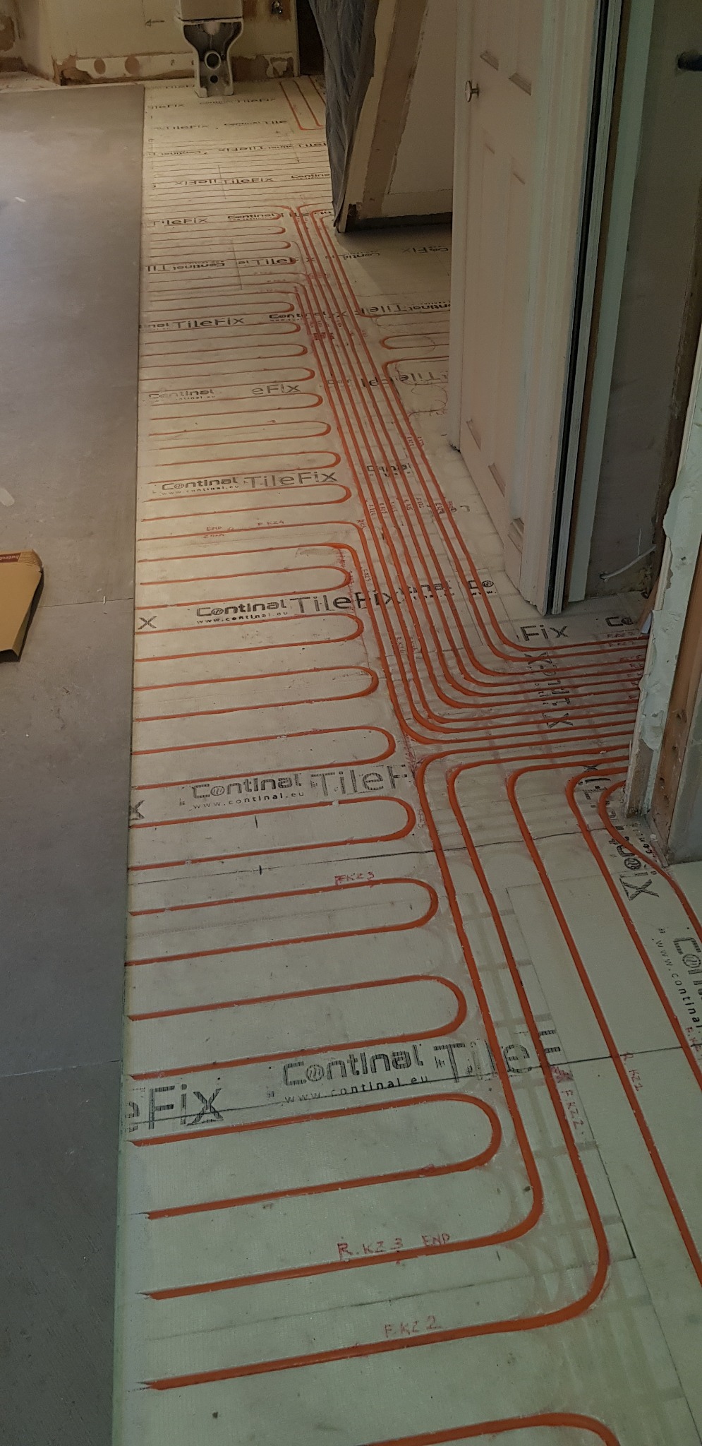 Instalacja ogrzewania podłogowego z widocznymi czerwonymi przewodami grzewczymi na specjalnej macie, przygotowanie do wylewki lub położenia płytek w trakcie remontu łazienki.