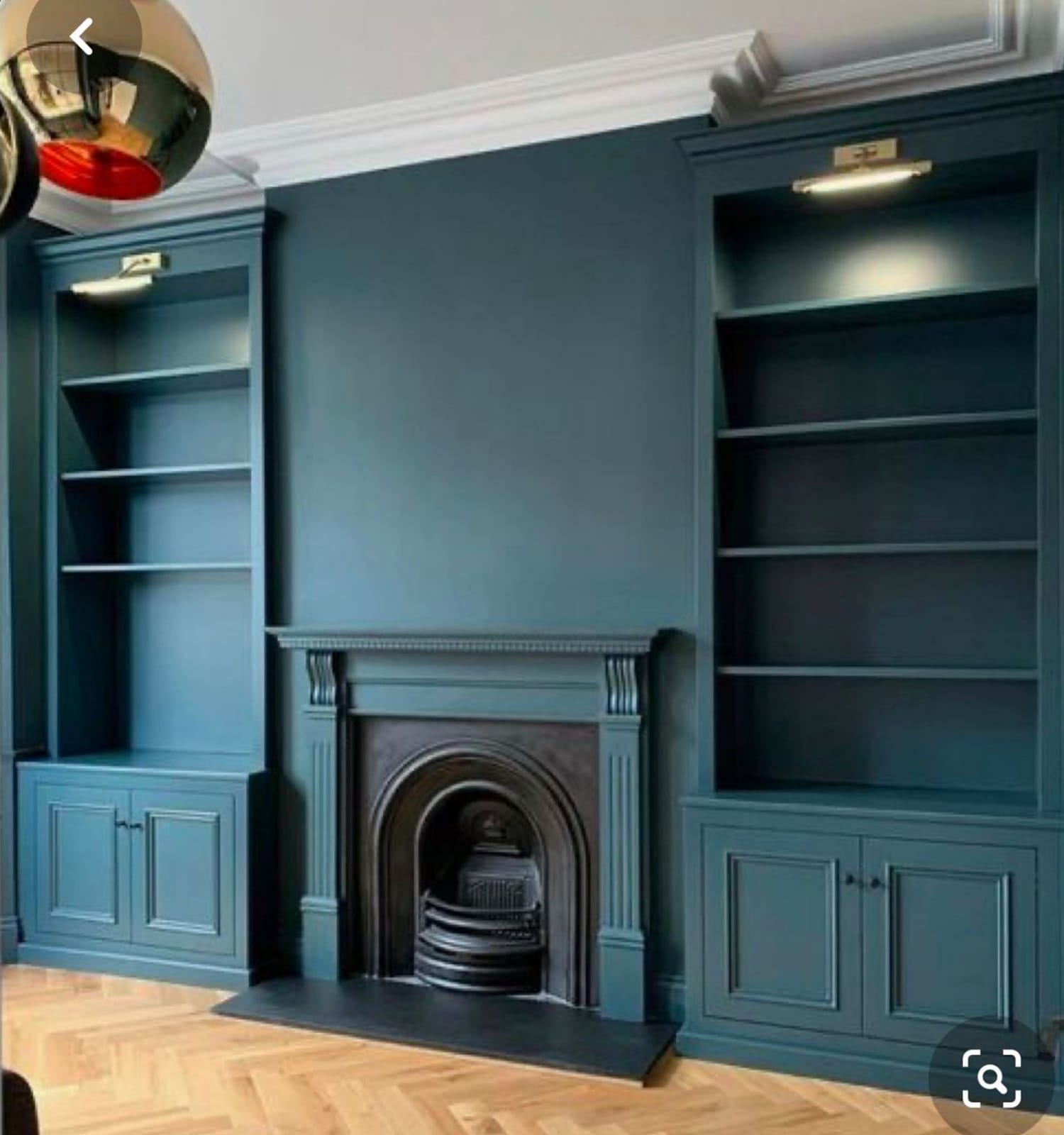 Elegancki salon z zabudowanymi regałami i kominkiem w odcieniach morskiej zieleni, parkiet w jodełkę, oświetlenie punktowe nad półkami, minimalistyczny design.