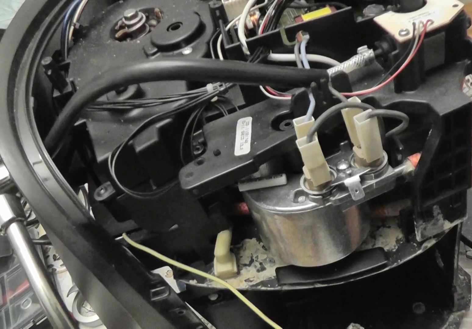 Wnętrze kuchenki mikrofalowej z widocznymi elementami elektrycznymi, przewodami i zabrudzeniami, sugerujące naprawę lub serwis.