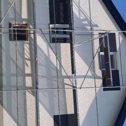 Usługi remontowo budowlane - Dom jednorodzinny w trakcie prac elewacyjnych, widoczne rusztowania i okna zabezpieczone folią.