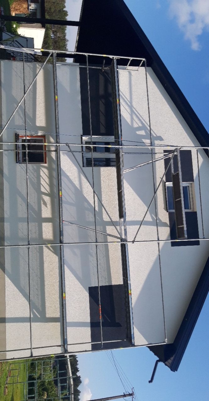 Dom jednorodzinny w trakcie prac elewacyjnych, widoczne rusztowania i okna zabezpieczone folią.