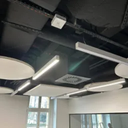 Nowoczesny sufit biurowy z czarną instalacją, okrągłymi i kwadratowymi panelami akustycznymi oraz liniowym oświetleniem LED.