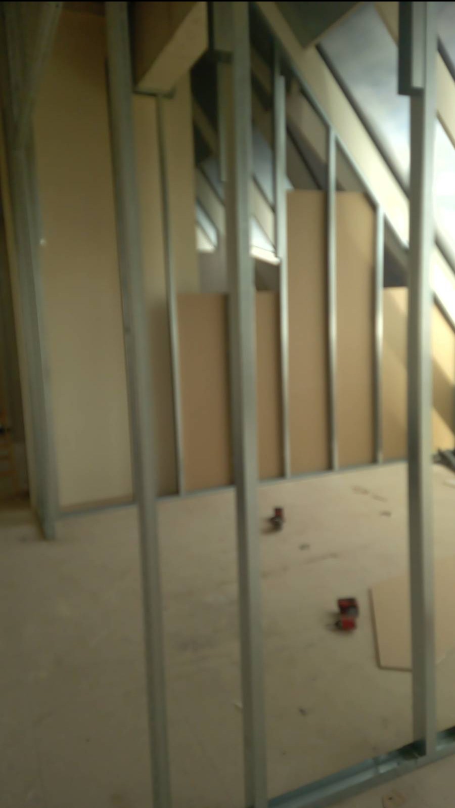 Konstrukcja szkieletowa z profili metalowych i płyt kartonowo-gipsowych w surowym stanie, widoczne wkręty i fragment poddasza.