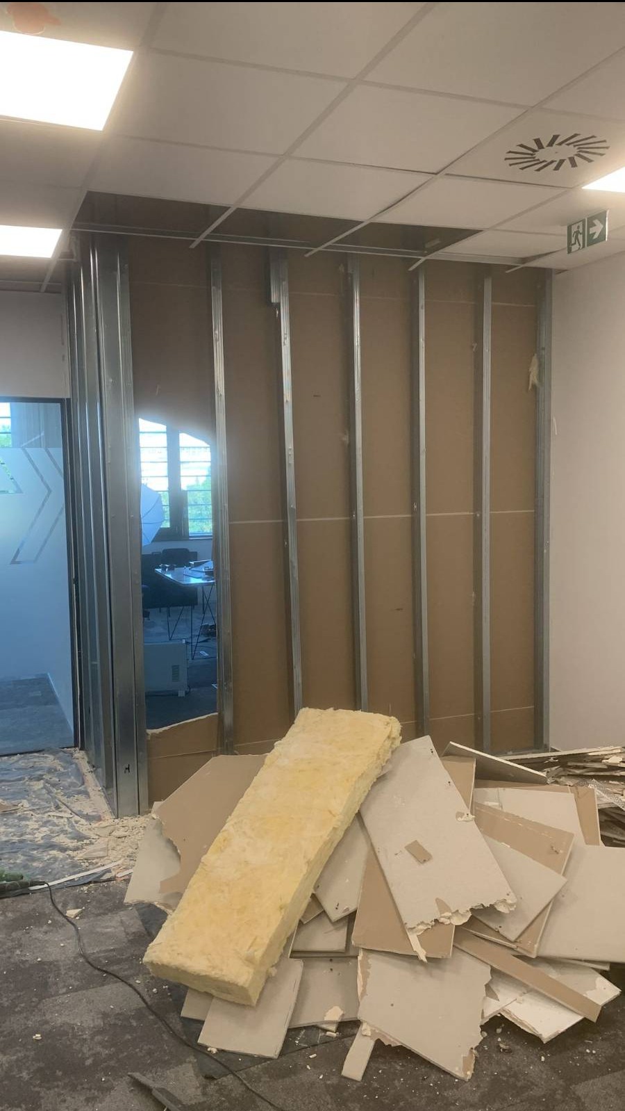 Montaż ścianki działowej z płyt karton-gips: widoczne metalowe profile, płyty karton-gips, izolacja z wełny mineralnej oraz pozostałości po cięciu płyt na podłodze.