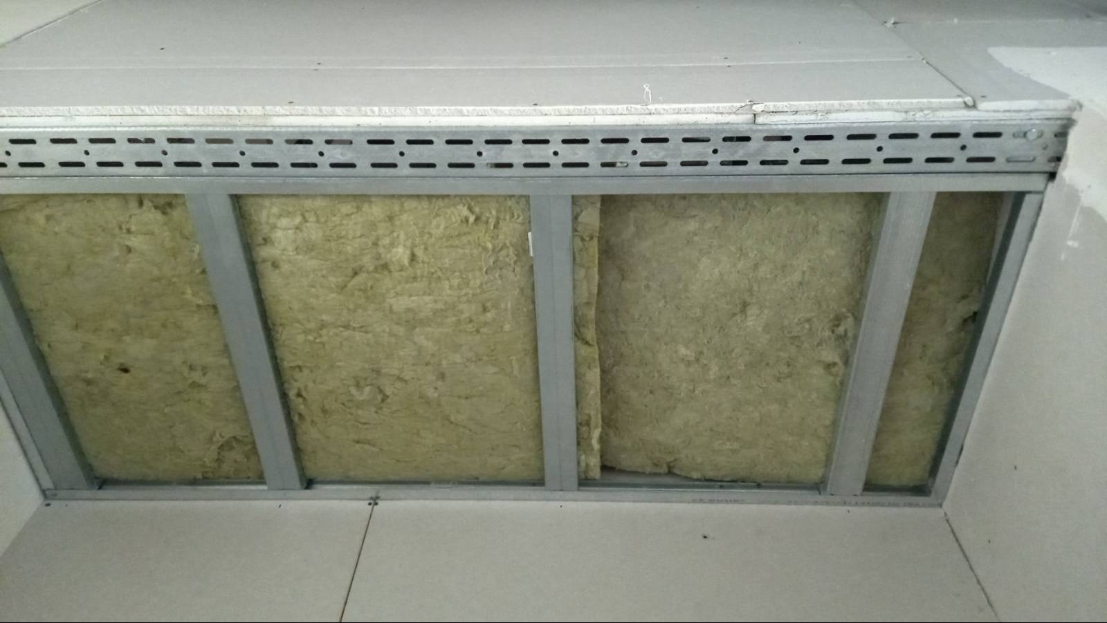 Konstrukcja sufitu podwieszanego z płyt kartonowo-gipsowych z widoczną wełną mineralną jako izolacją, metalowe profile w trakcie montażu.