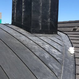 Usługi Blacharsko-Dekarskie Andrzej Kasperek - Szary dach z blachy na budynku w Szaflarach z widocznym kominem obłożonym blachą. Na dachu leży zwitek białego materiału.