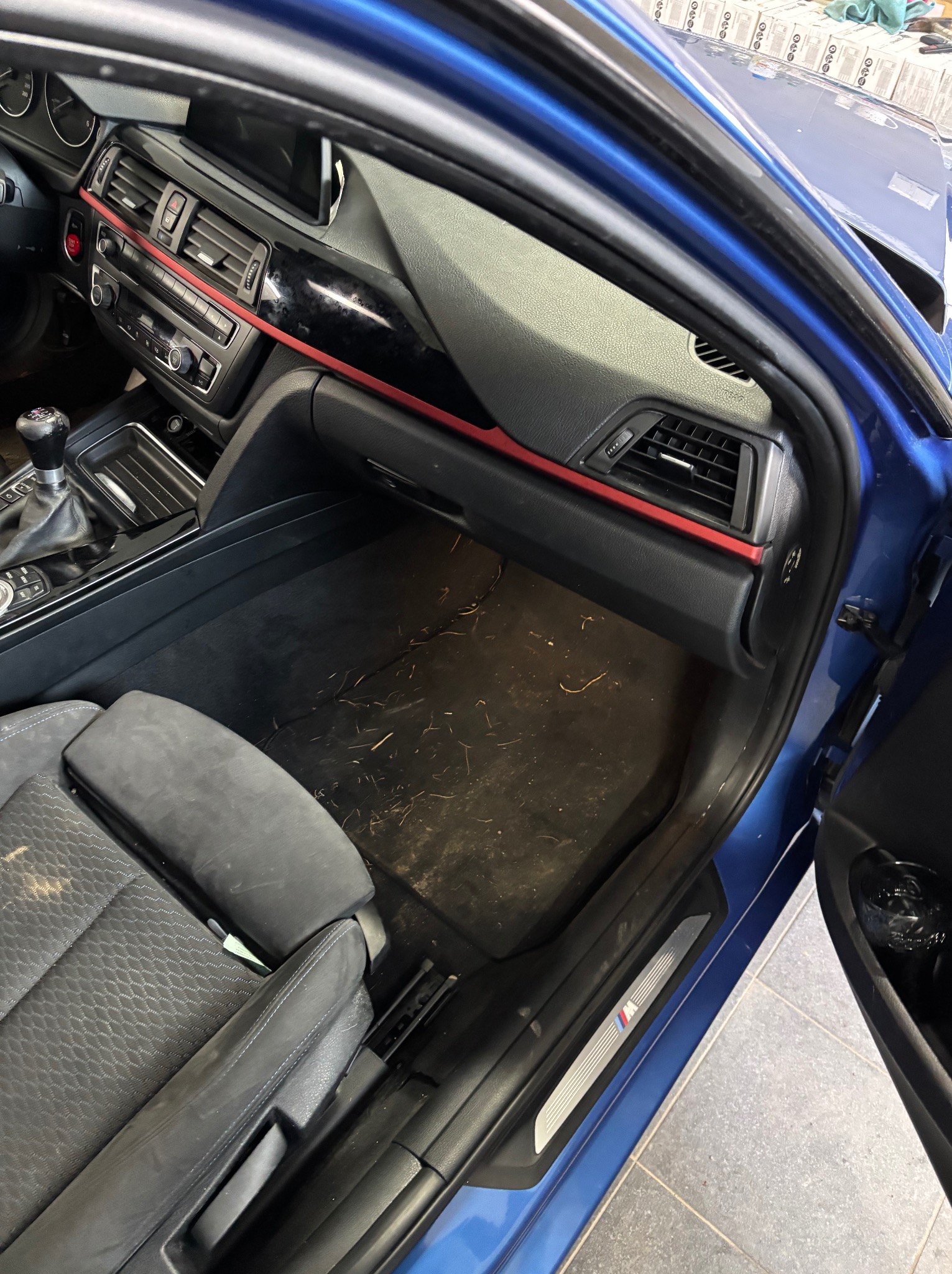 Wnętrze brudnego, niebieskiego samochodu BMW z widocznymi zabrudzeniami na dywaniku i siedzeniu kierowcy, sugerujące potrzebę czyszczenia.