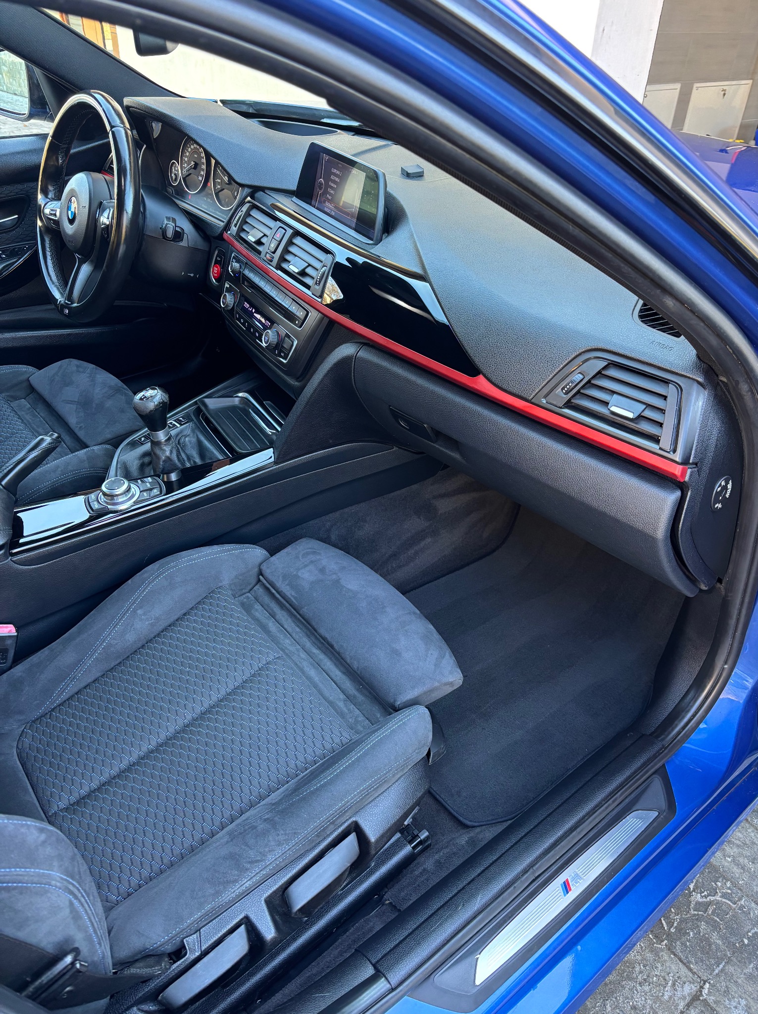 Wnętrze niebieskiego BMW serii 3 po detailingu: czarne, welurowe fotele, deska rozdzielcza z czerwonym akcentem, czysta podłoga. Widok z zewnątrz auta.