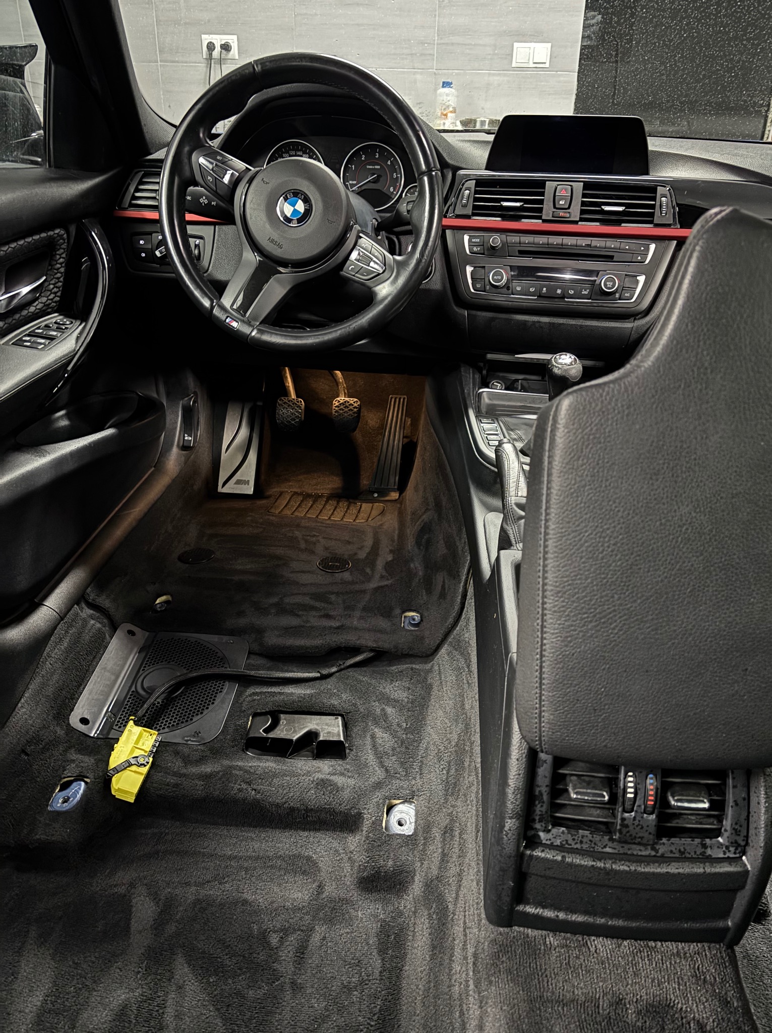 Wnętrze samochodu BMW w trakcie czyszczenia. Widoczny kokpit, kierownica, fotele i częściowo zdemontowana podłoga z elementami instalacji elektrycznej.