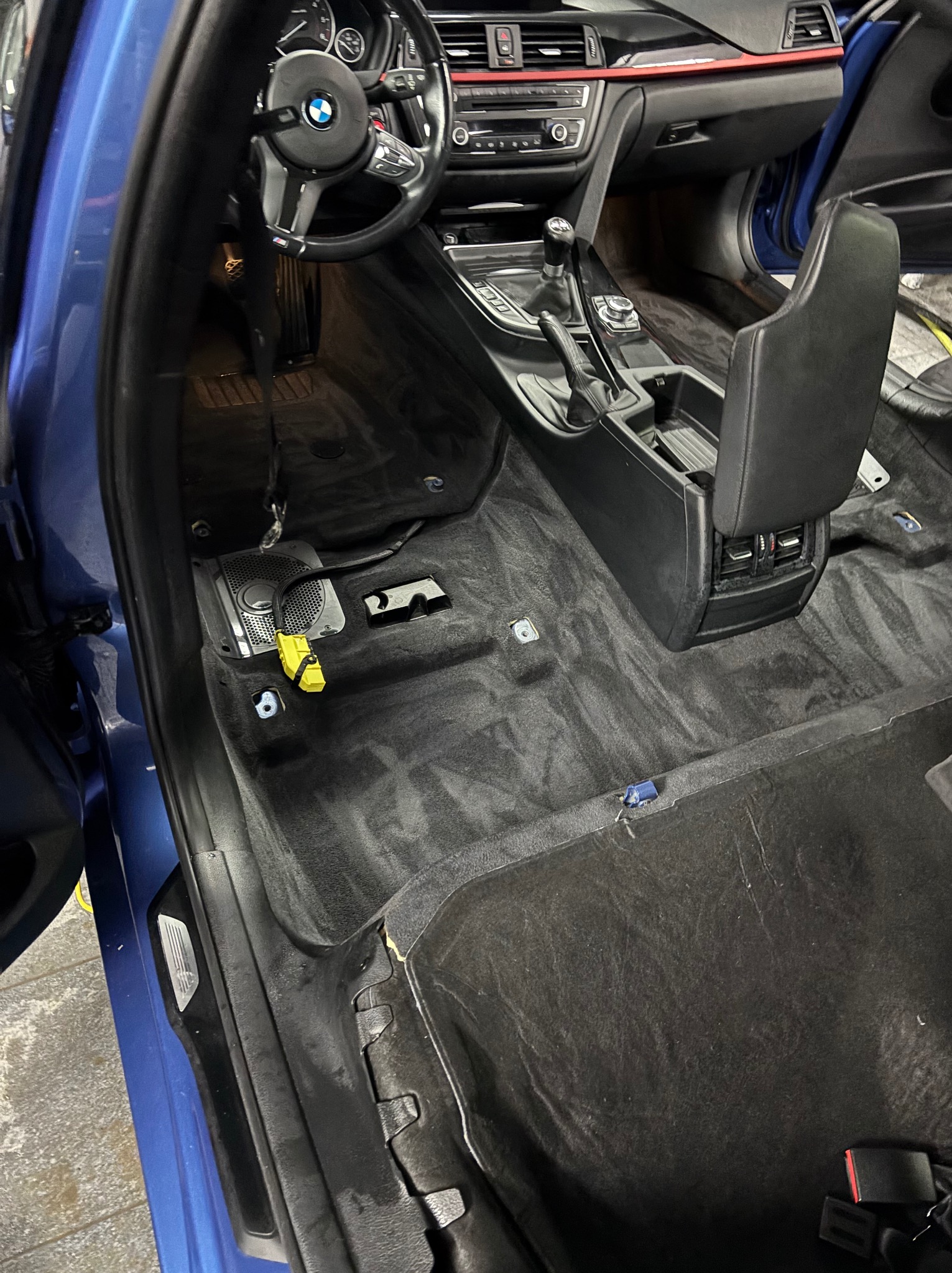 Wnętrze niebieskiego BMW serii 3 w trakcie czyszczenia. Wyjęte fotele, widoczna podłoga z elementami demontażu. Detailing wnętrza w trakcie realizacji.