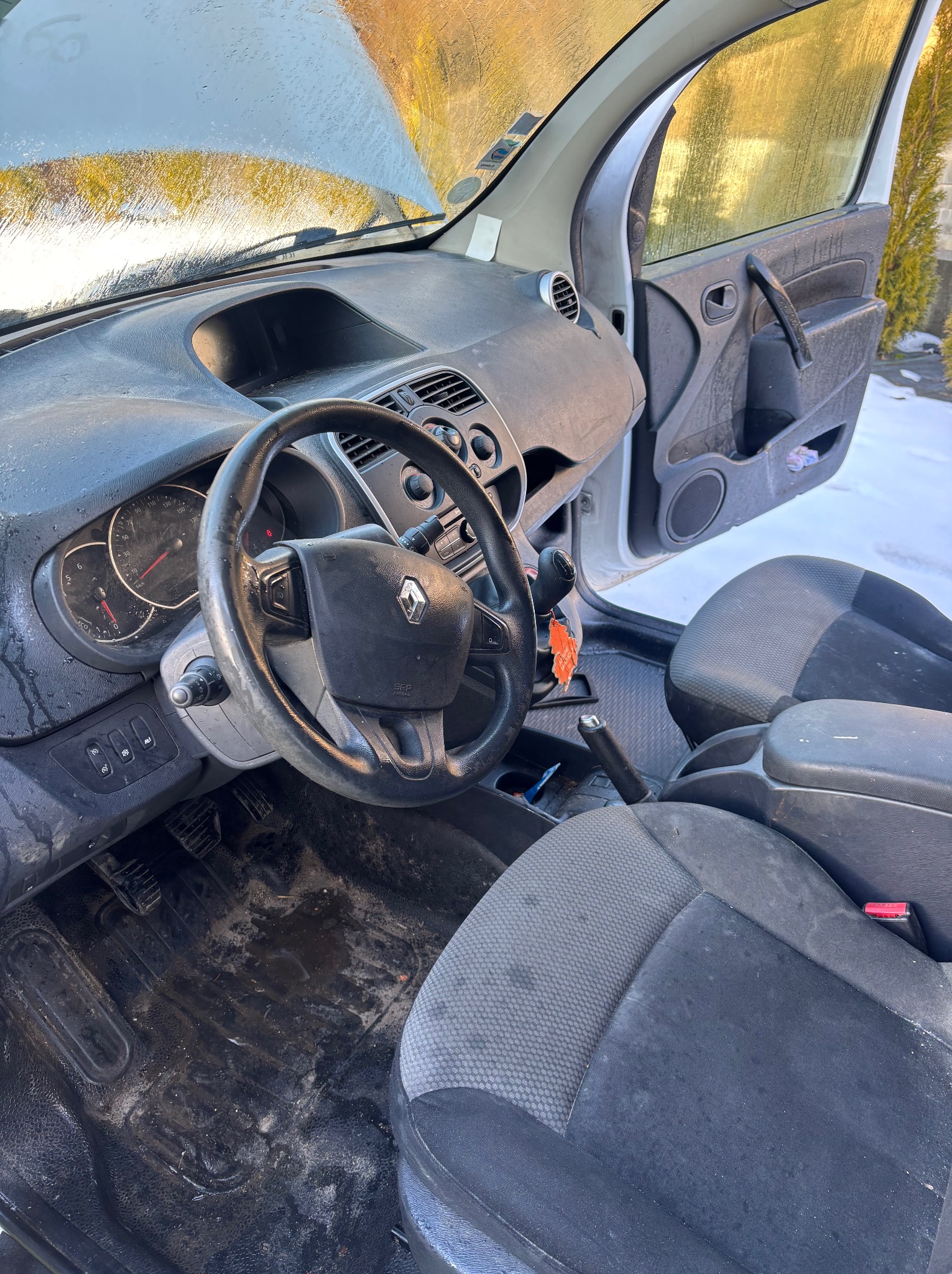 Wnętrze brudnego samochodu Renault Kangoo z otwartą maską i drzwiami, widoczne zabrudzenia na siedzeniach, podłodze i desce rozdzielczej. Ślady wody na szybach.