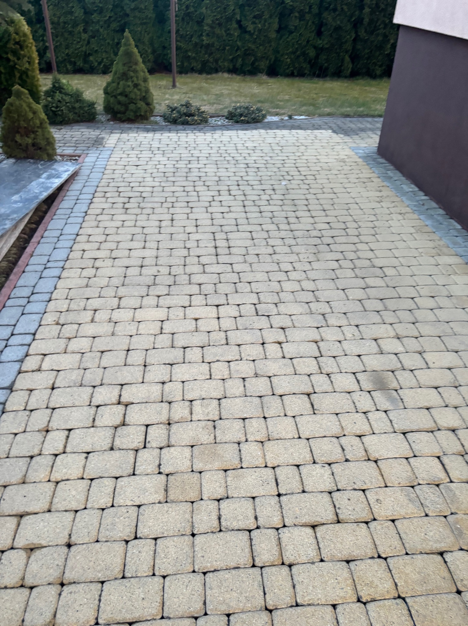 Ułożona kostka brukowa w Podegrodziu, widok z góry. Beżowa kostka z szarym obramowaniem, zielone krzewy w tle. Precyzyjne ułożenie, równa powierzchnia.
