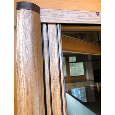 Detale drewnianej ramy drzwi przesuwnych z widocznym systemem prowadnic i fragmentem wnętrza w tle.