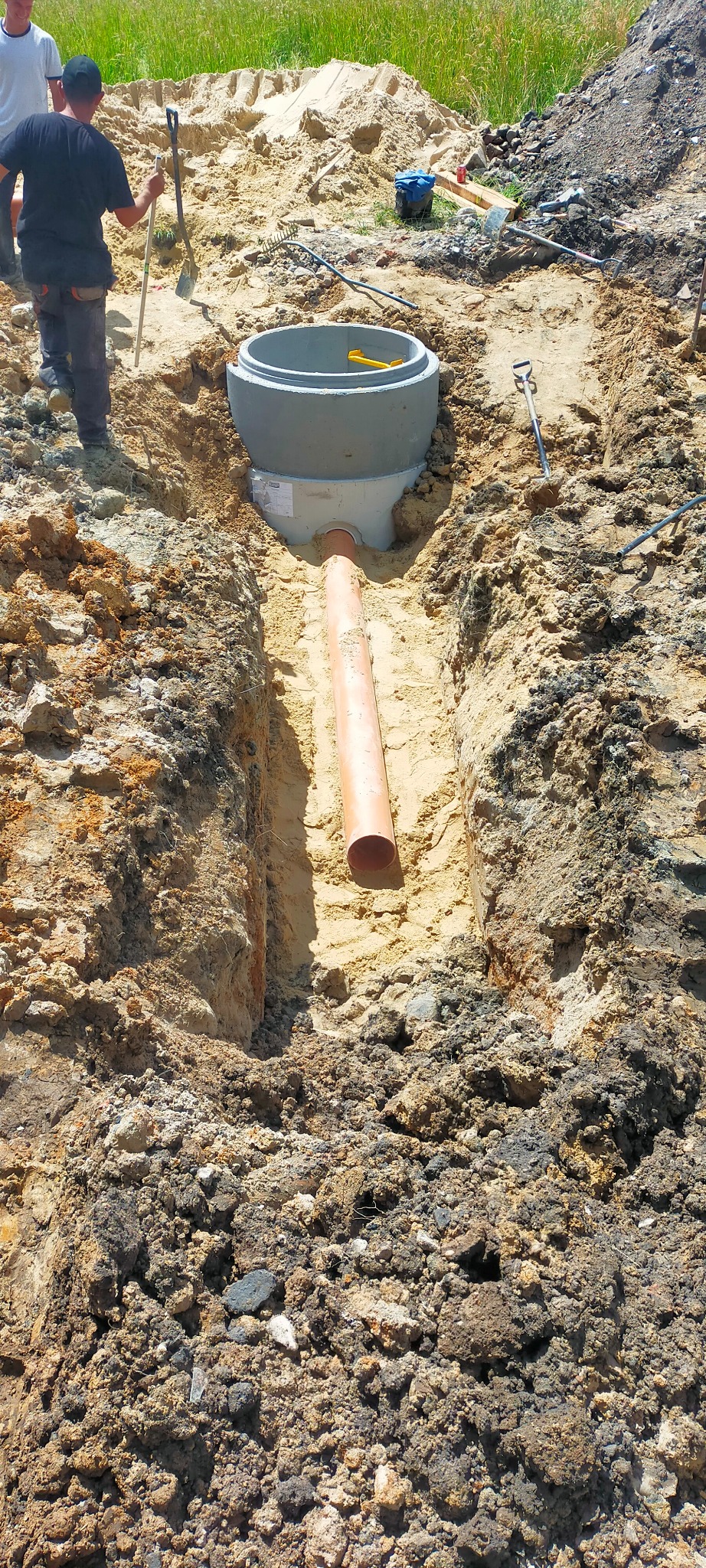 Montaż betonowego zbiornika z rurą w wykopie w Rudzie Śląskiej, widoczne narzędzia i pracownicy w tle.