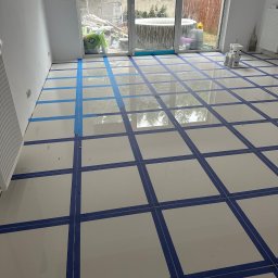 valentyn haliev - Białe płytki podłogowe zabezpieczone niebieską taśmą malarską tworzącą kwadratowy wzór przed fugowaniem, widok na patio z jacuzzi.