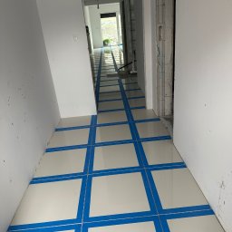 valentyn haliev - Korytarz w trakcie prac wykończeniowych: białe ściany, ułożona jasna podłoga z płytek zabezpieczona niebieską taśmą wyznaczającą wzór, widoczne surowe wykończenie ościeżnicy.