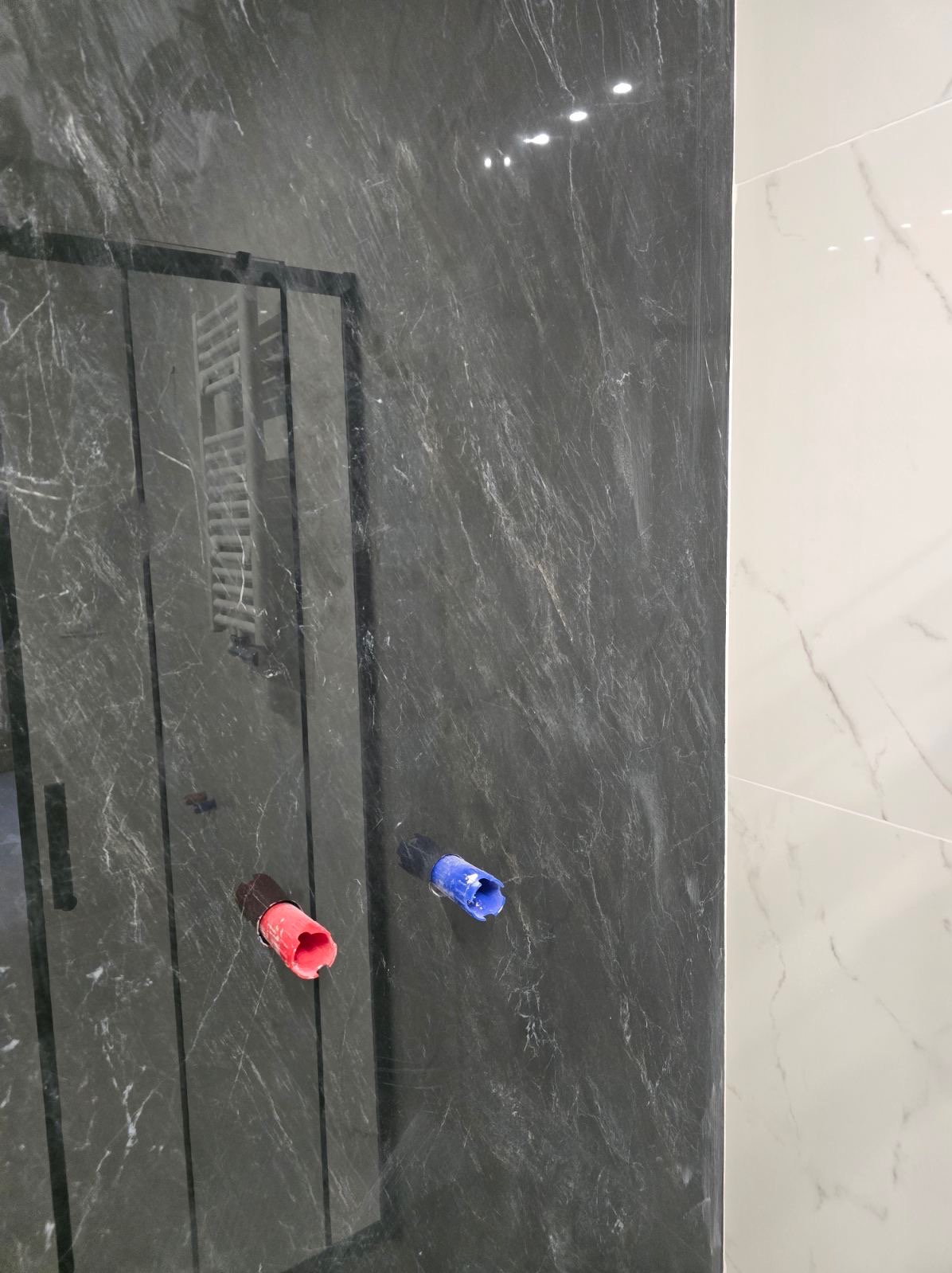 Przygotowanie do podłączenia armatury w łazience wykończonej płytami imitującymi marmur, widoczne rury z zaślepkami w kolorze czerwonym i niebieskim.