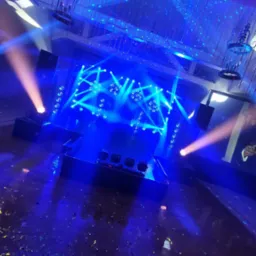 Scena oświetlona niebieskimi światłami i reflektorami, z konfetti na podłodze i dekoracjami wiszącymi z sufitu.