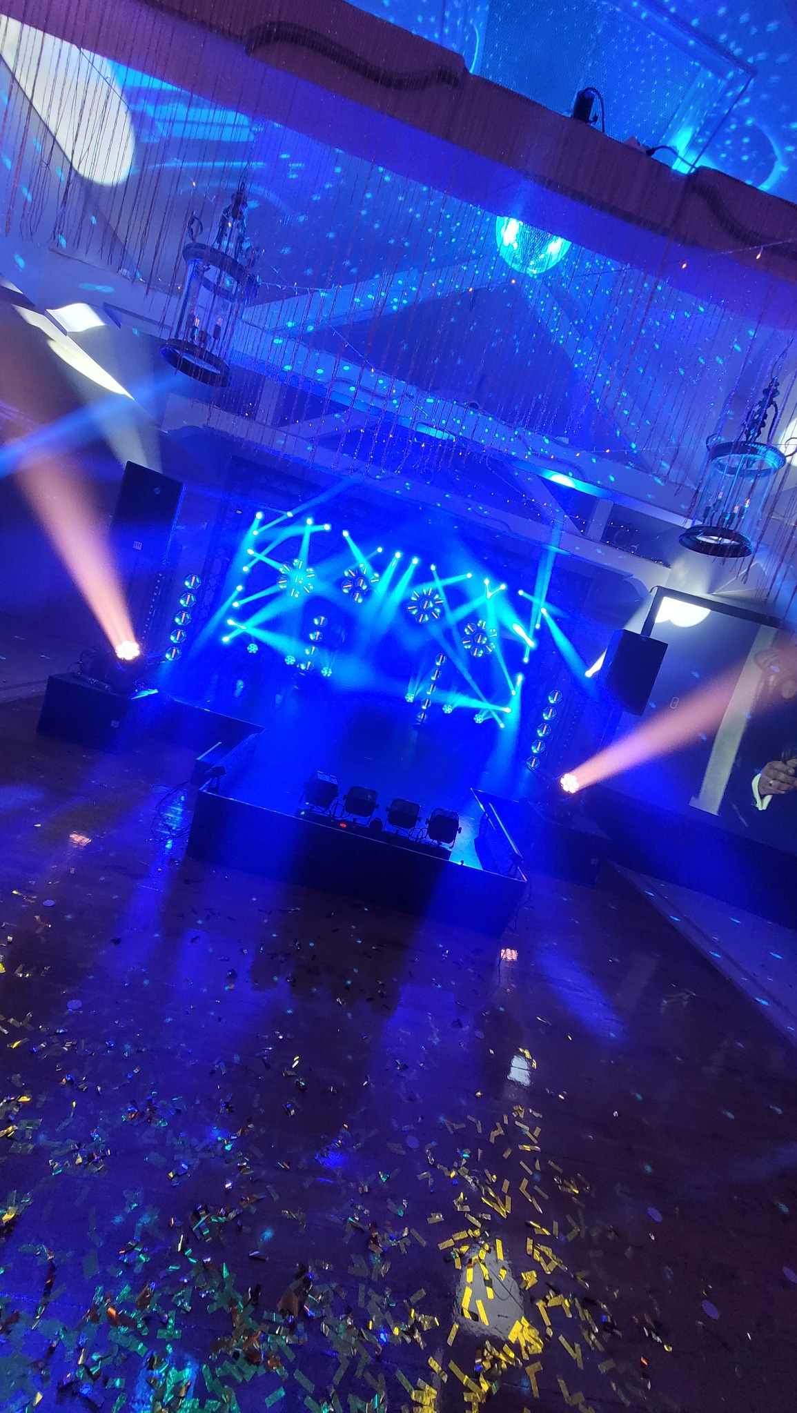 Scena oświetlona niebieskimi światłami i reflektorami, z konfetti na podłodze i dekoracjami wiszącymi z sufitu.