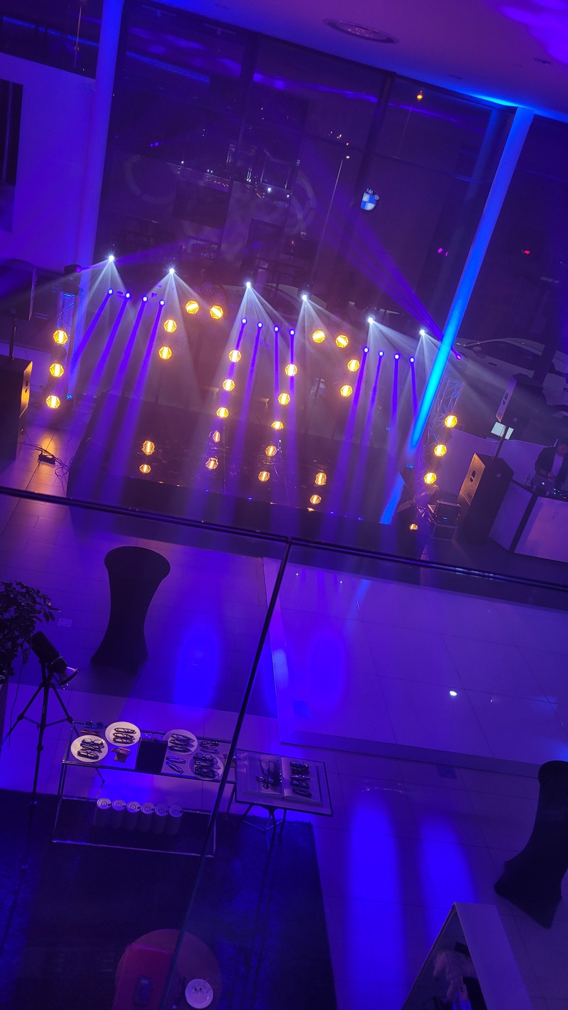 Scena oświetlona reflektorami w kolorach fioletu i bieli, widok z góry przez szklaną taflę, w tle widoczne zaplecze z cateringiem i sprzętem.