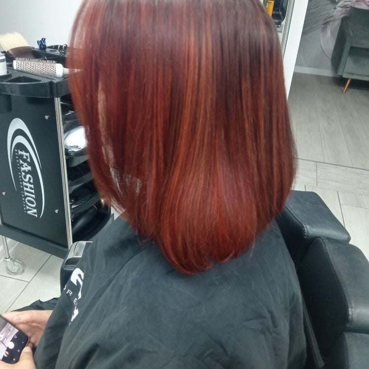 Świeżo ufarbowane, miedziano-rude włosy do ramion, widoczne od tyłu, z delikatnymi refleksami, na tle czarnego wózka fryzjerskiego z logo 'Fashion'.