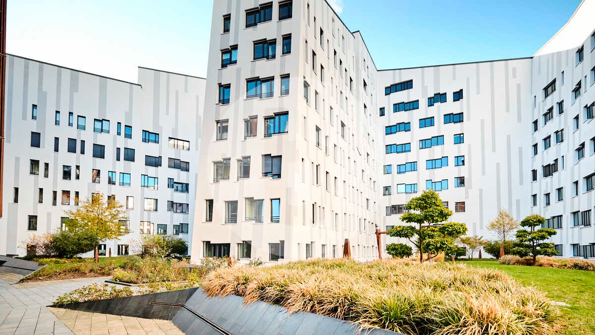 Nowoczesny budynek mieszkalny z licznymi oknami, otoczony zielenią i niską roślinnością ozdobną, Węgierki.